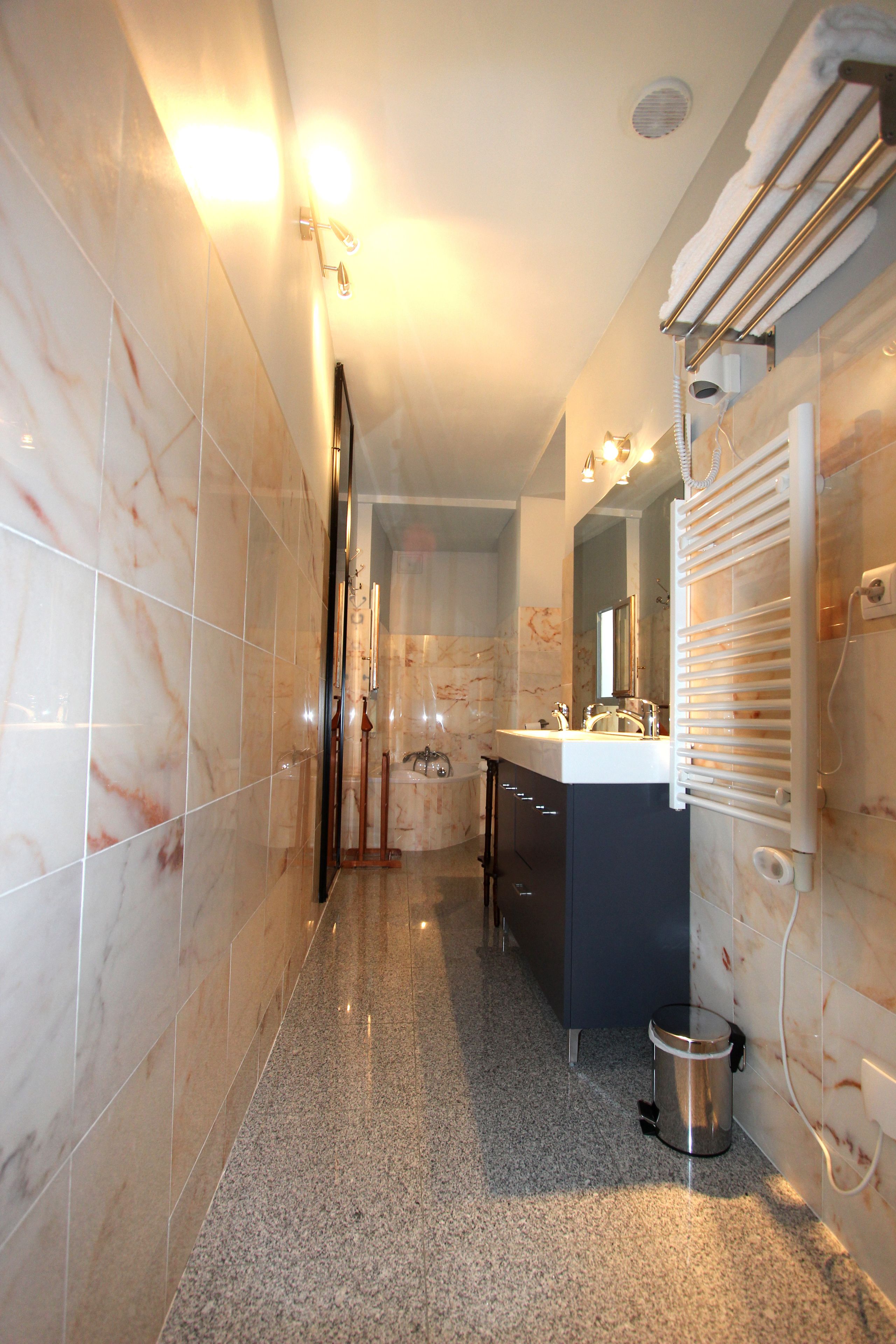 A modern bathroom with marble tiles, a sink, a mirror, a towel rack, and a shower area.