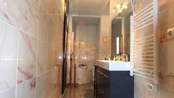 A modern bathroom with marble tiles, a sink, a mirror, a towel rack, and a shower area.