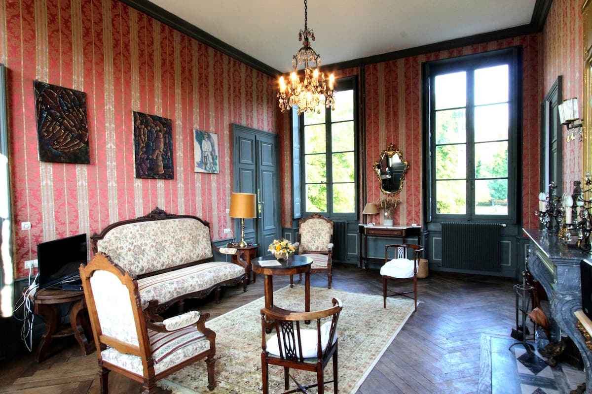 Une pièce comprenant un canapé, des fauteuils, une table ornée de fleurs, un lustre et une cheminée.