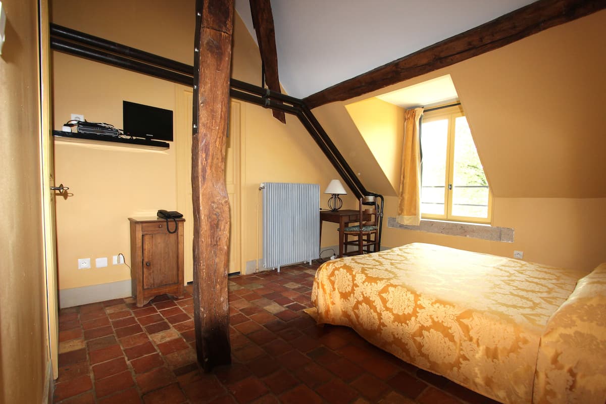 Une chambre avec un plafond en pente, un lit, un bureau, une chaise et une fenêtre.