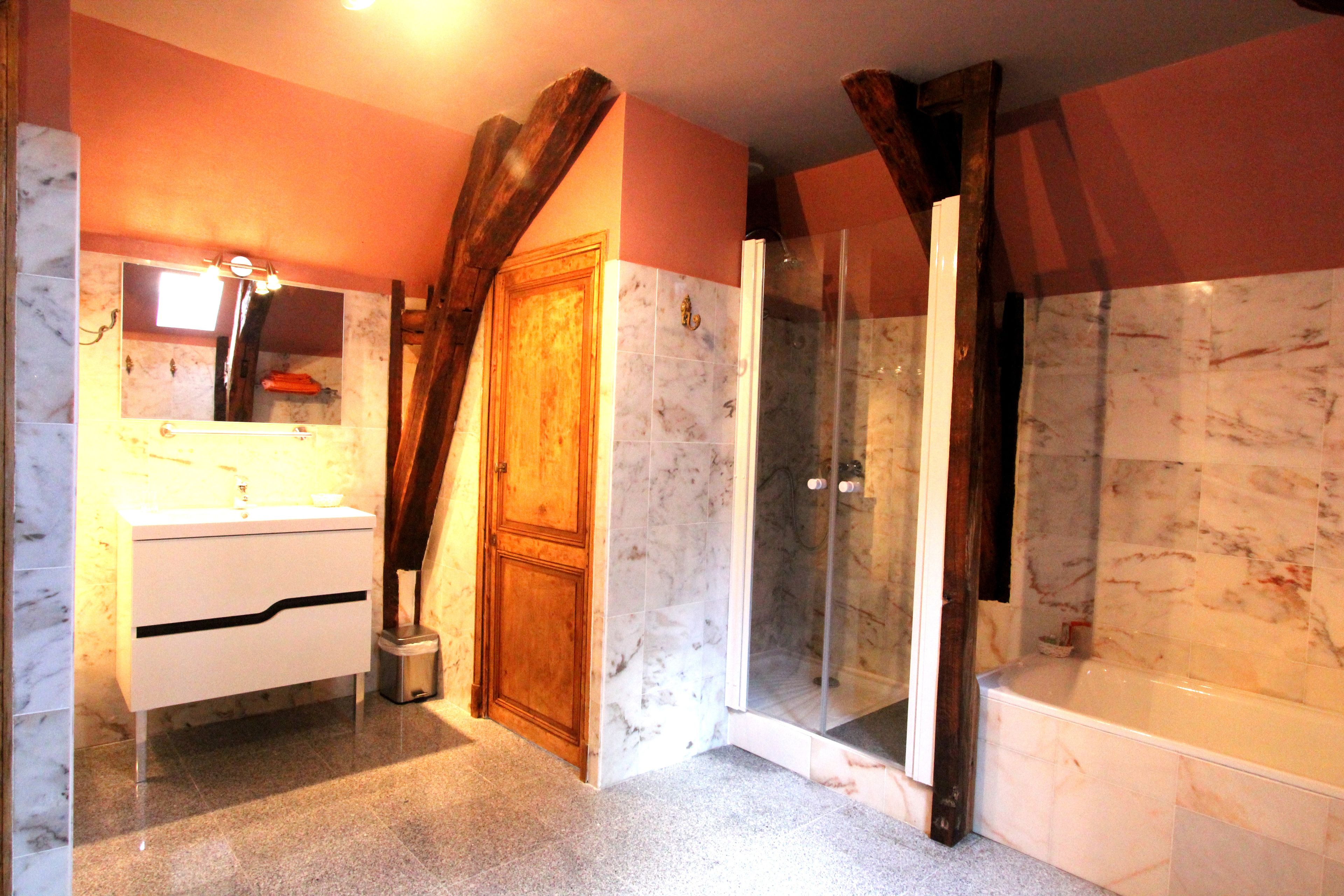 A bathroom with a marble sink, wooden door, and a glass shower enclosure.