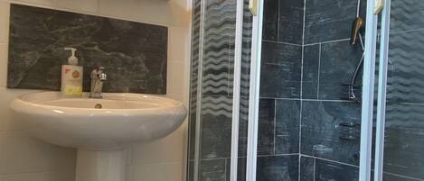 A bathroom with a pedestal sink, a glass-enclosed shower, and a mirror above the sink.