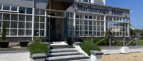 Het uiterlijk van Marlborough Hotel, met een opvallende ingang, een overdekte veranda en een grindpad dat naar de deur leidt.