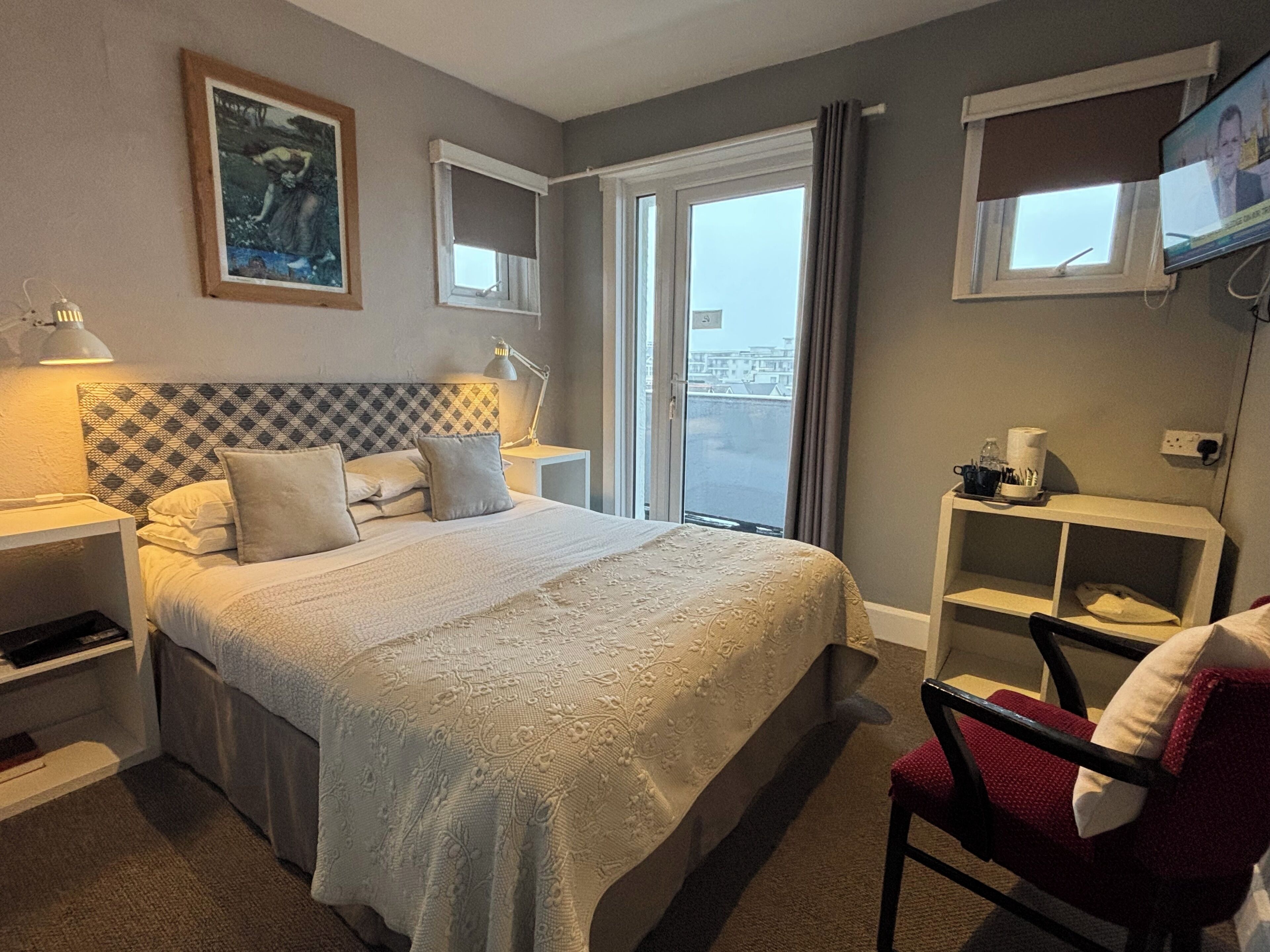 A hotel room with a bed, bedside tables, a chair, a TV, and a window with a view.