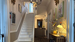 A hallway with a staircase, a kitchen area, and a table with a lamp and flowers. - Marlborough Hotel (Shanklin)