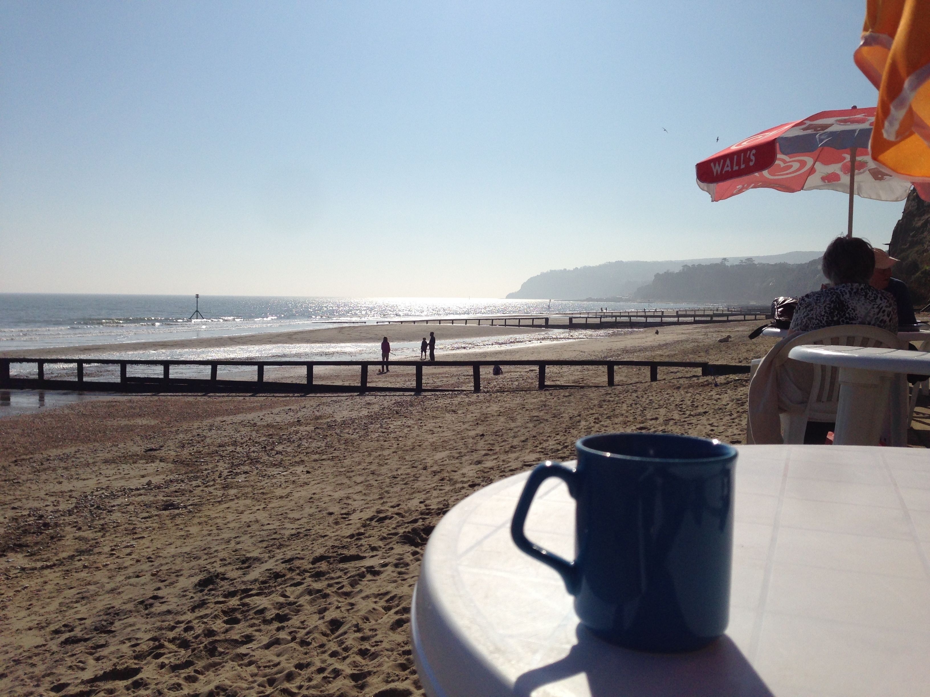 A beach view with a clear sky, a sandy shore, and a wooden pier.