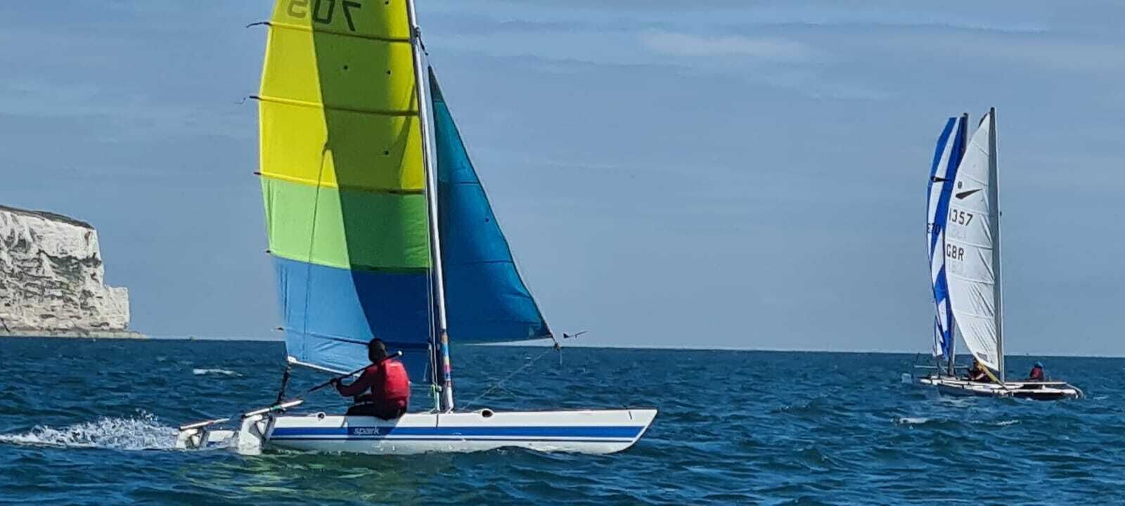 A sailboat with a multicolored sail and a person in a red life jacket.