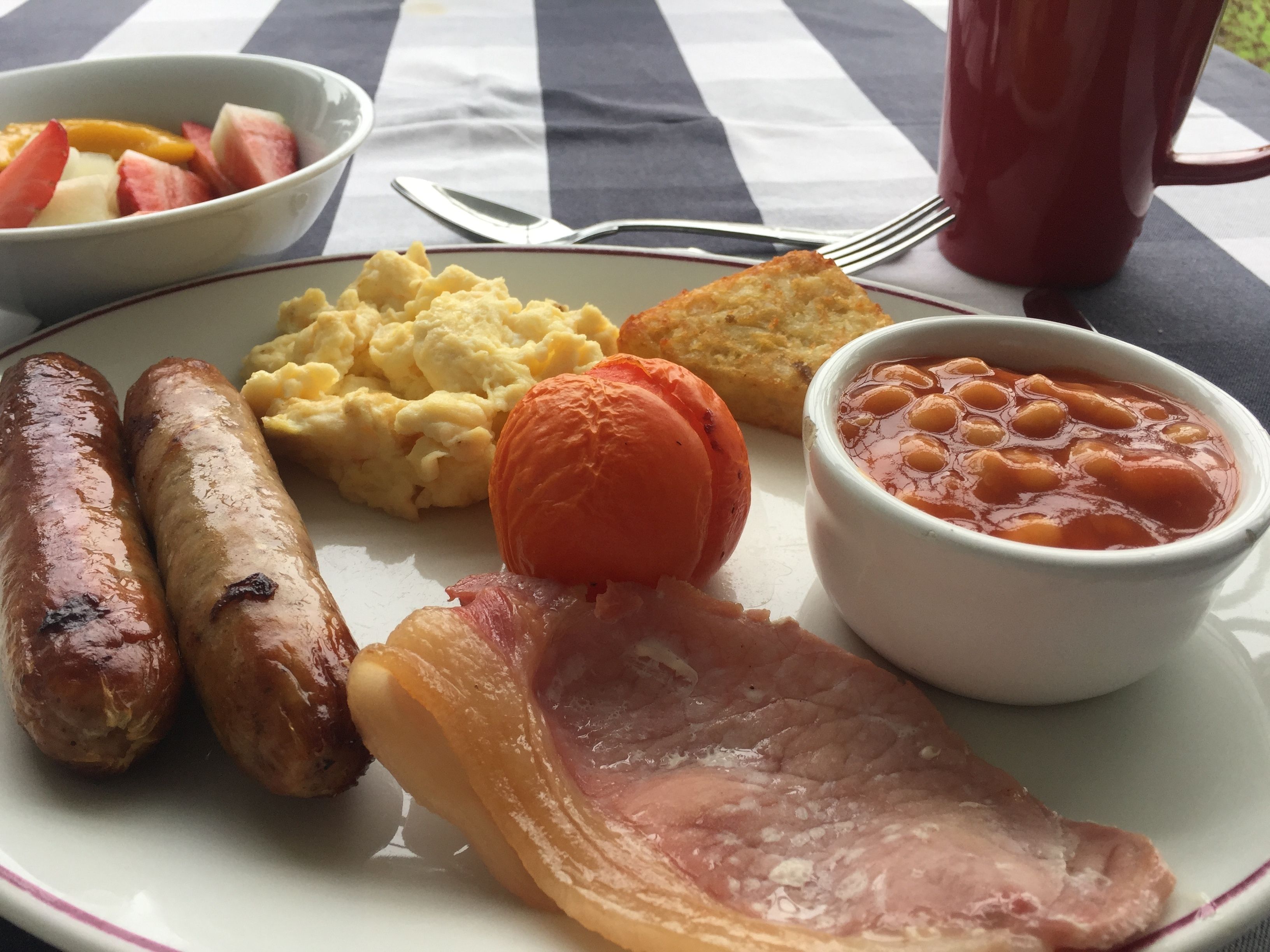 A plate with sausages, scrambled eggs, baked beans, a baked potato, and a ham slice.