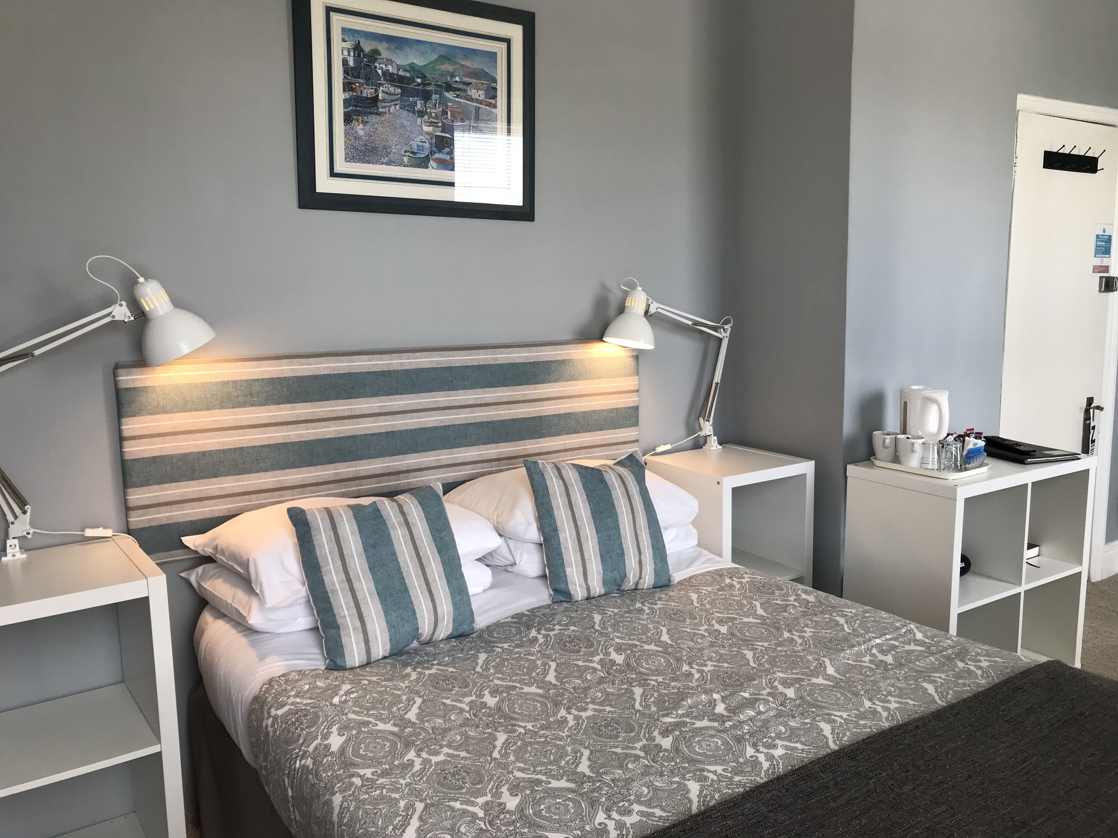 A neatly arranged hotel room with a striped headboard, a patterned bedspread, and two bedside tables with lamps.