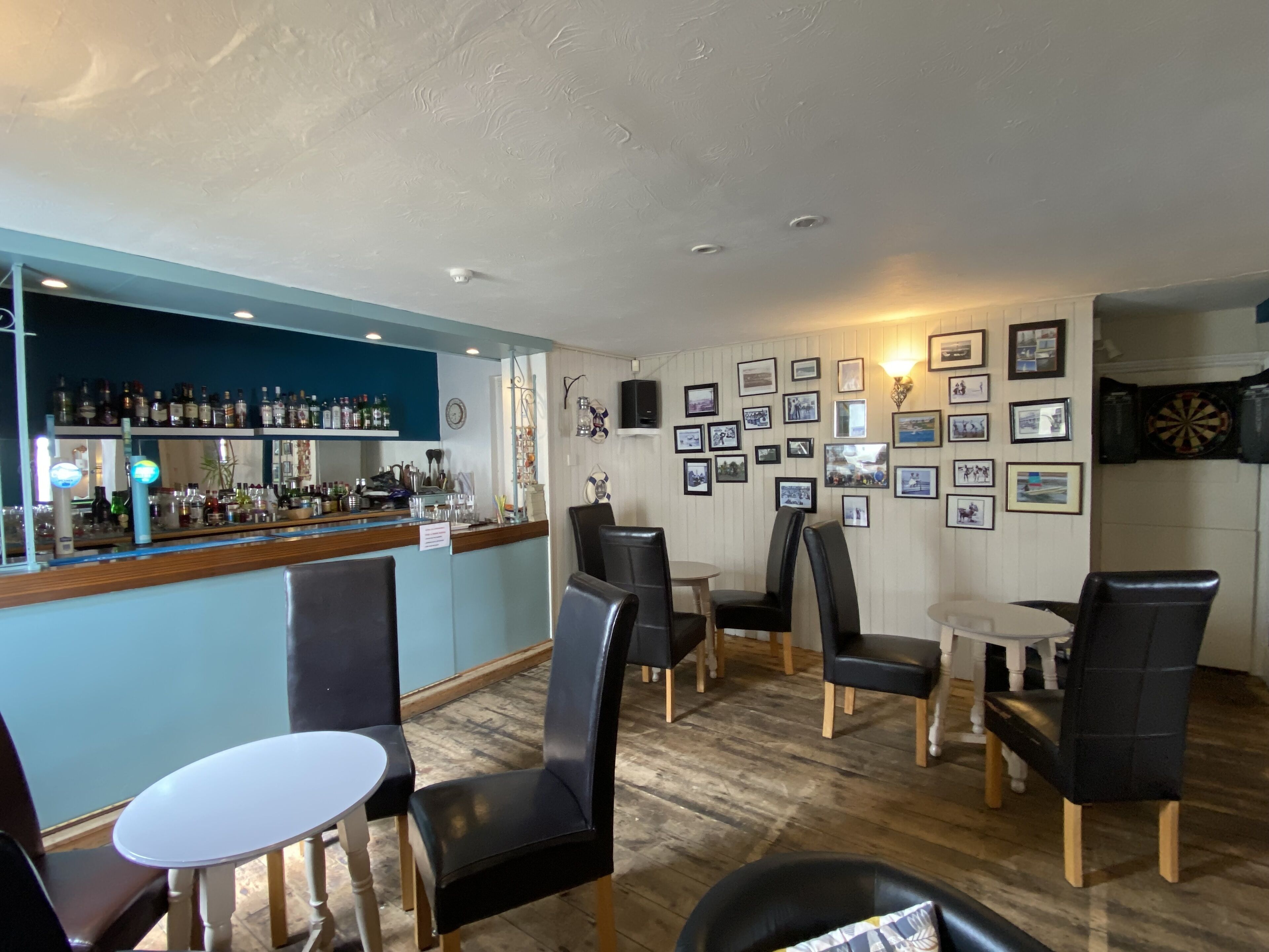 Un espace bar avec un comptoir, des étagères remplies de bouteilles et des tableaux encadrés accrochés au mur.