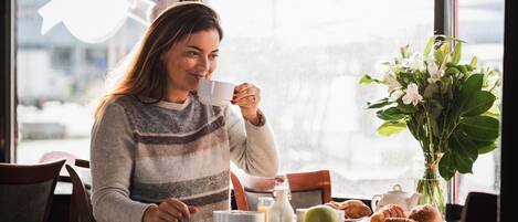 A person sitting at a table with a cup, a vase of flowers, and pastries.