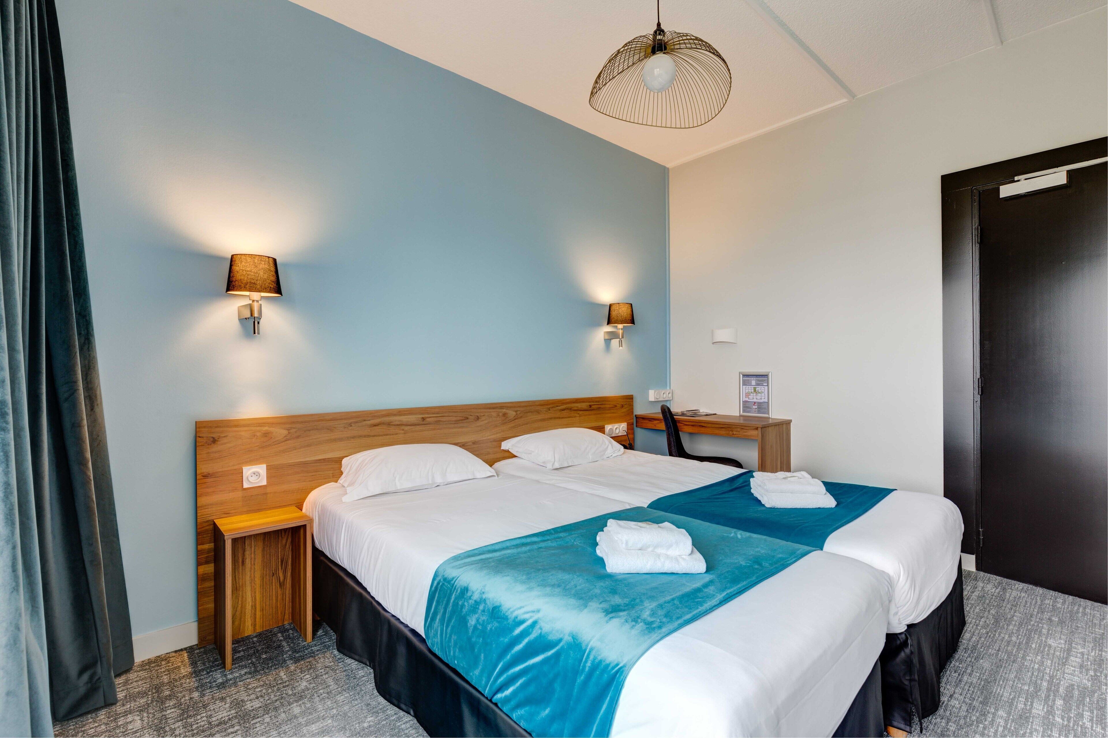Una habitación de hotel con una cama grande, dos mesitas de noche, un cabecero de madera y dos lámparas de pared.