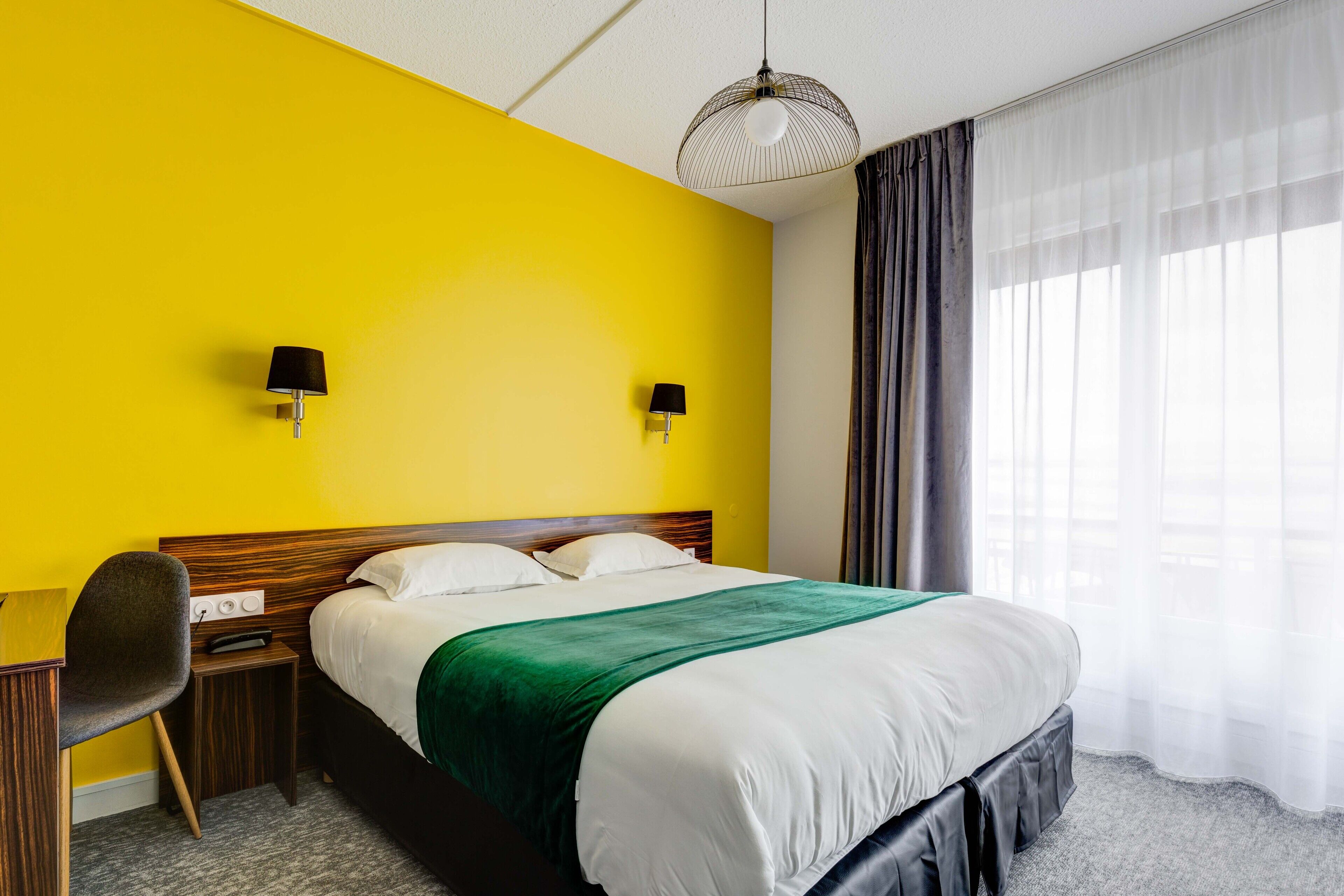 Habitación de hotel con una cama grande, dos lámparas de noche, un escritorio con silla y una ventana con cortinas.