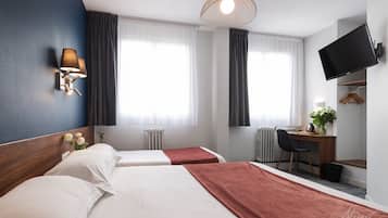 A hotel room with two beds, a desk, a chair, a TV, and a window with curtains.