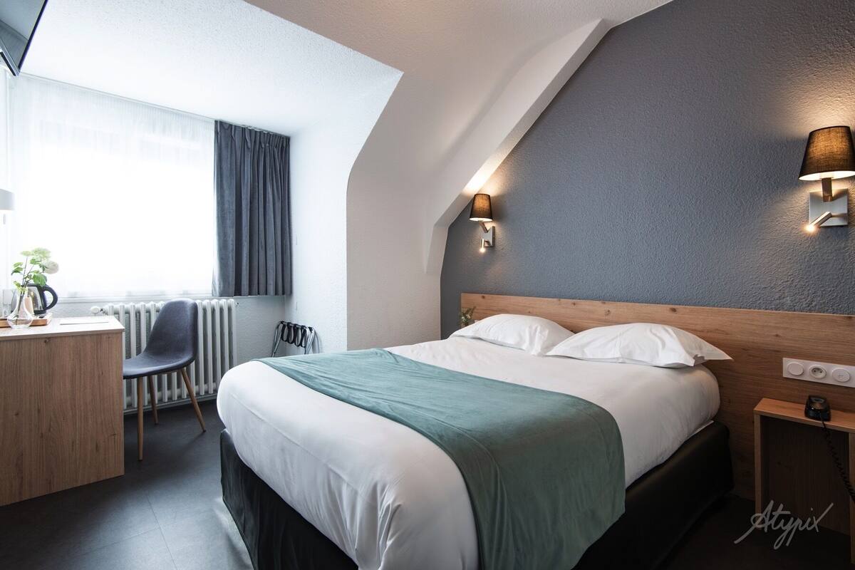 Una habitación de hotel moderna con cama, mesita de noche, lámpara y escritorio con silla.
