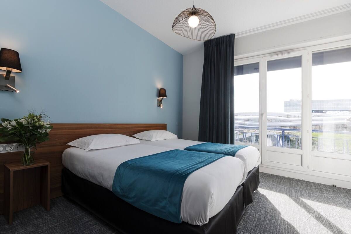 Habitación de hotel con una cama grande, una mesita de noche, una lámpara y vistas amplias de la ciudad.