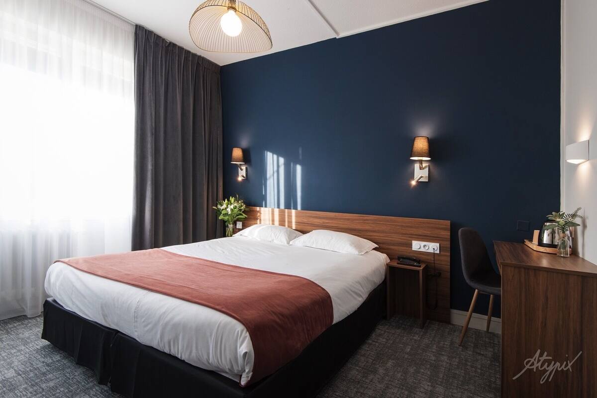 Una habitación de hotel moderna con una cama grande, dos mesitas de noche, un escritorio y una silla.