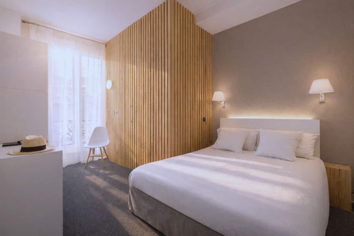 A modern hotel room with a large bed, two bedside lamps, a wooden accent wall, a white desk, and a chair.