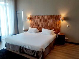 Una habitación de hotel con una cama grande, dos lámparas de noche, un cabecero de madera, una mesita de noche con un teléfono y un espejo grande.