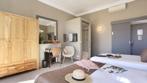 A hotel room with a wooden wardrobe, a desk with a chair, a bed with a magazine and a straw hat, and a door with a light switch. - La Villa Tosca (Cannes)