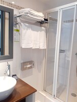 Un baño con cabina de ducha de vidrio, un lavabo con espejo y un perchero con toallas dobladas.
