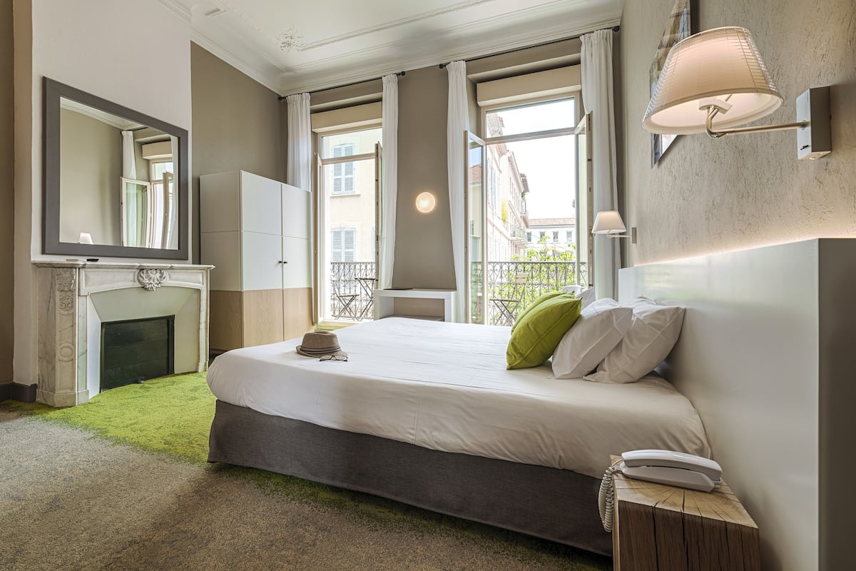 A modern hotel room with a large bed, a fireplace, a mirror, and a balcony view.
