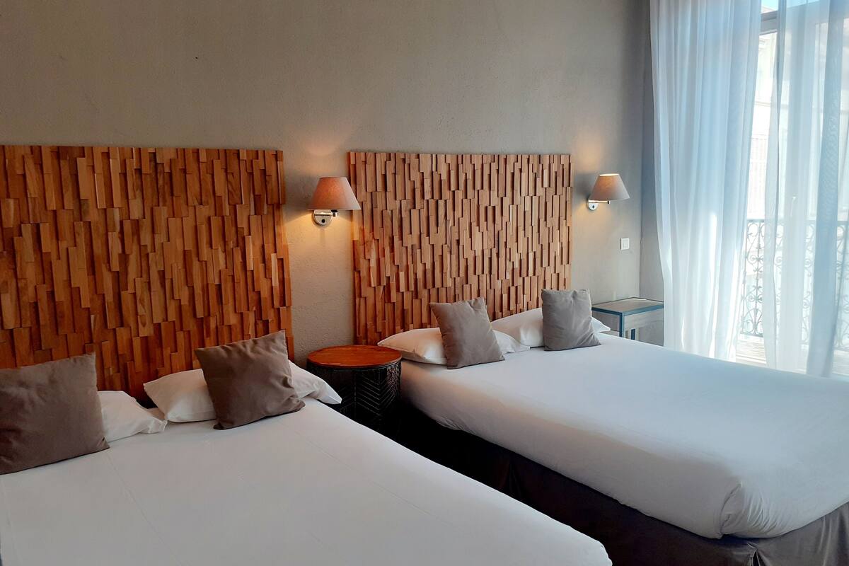 A hotel room with two beds, wooden headboards, bedside lamps, a round table, and a view of the outdoors.