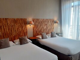 Een hotelkamer met twee bedden, houten hoofdborden, bedlampen, een ronde tafel en uitzicht op het omliggende landschap.