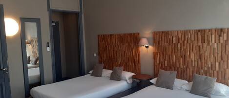 A hotel room with two beds, a wooden headboard, a bedside table, and a mirror.
