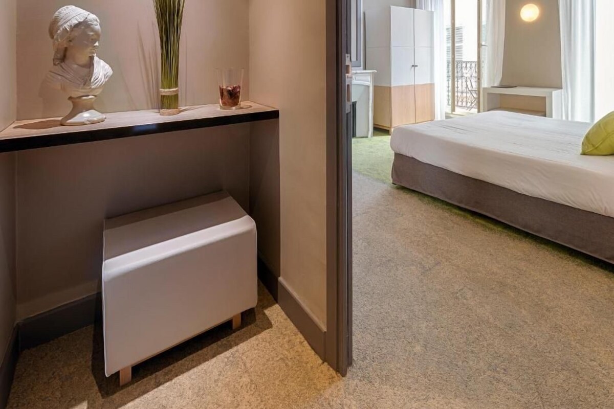 Una habitación de hotel moderna con una cama, un escritorio, una escultura de busto y una planta en maceta.