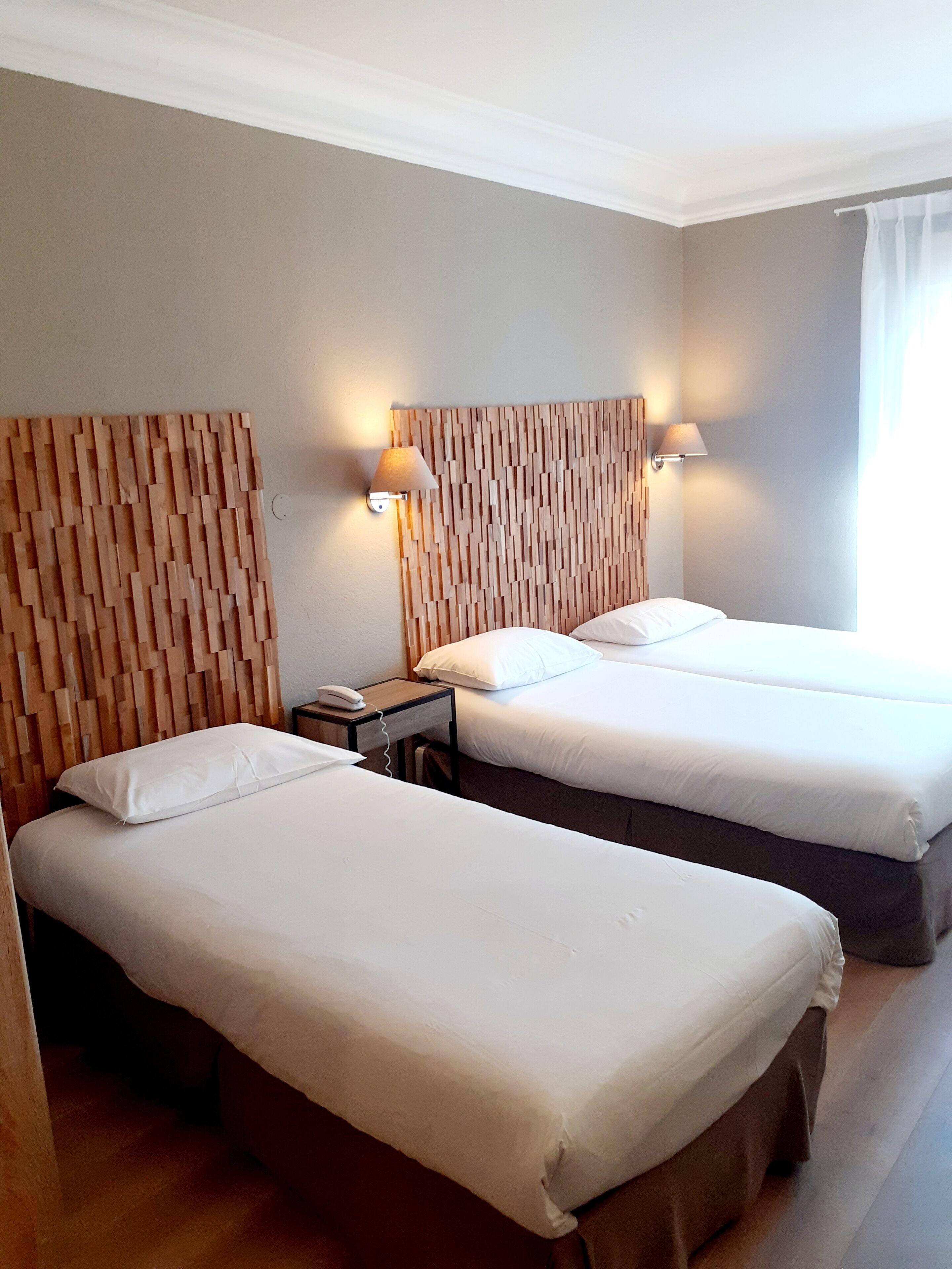 Une chambre d’hôtel avec deux lits, une tête de lit en bois, une table de chevet avec une lampe et un téléphone.