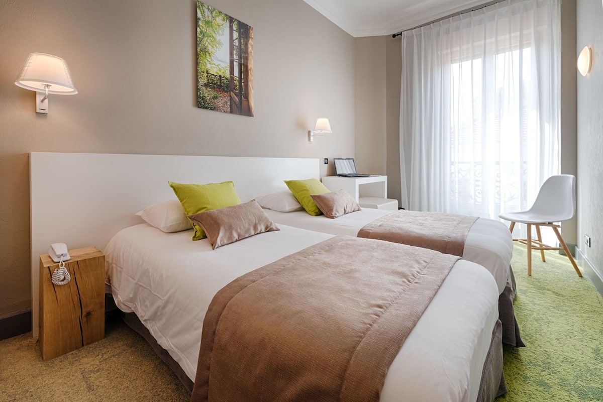 A hotel room with two beds, a desk, a chair, and a phone on a nightstand.