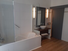 A modern bathroom with a glass-enclosed shower, a white bathtub, and a wooden vanity with a mirror and wall-mounted lights.