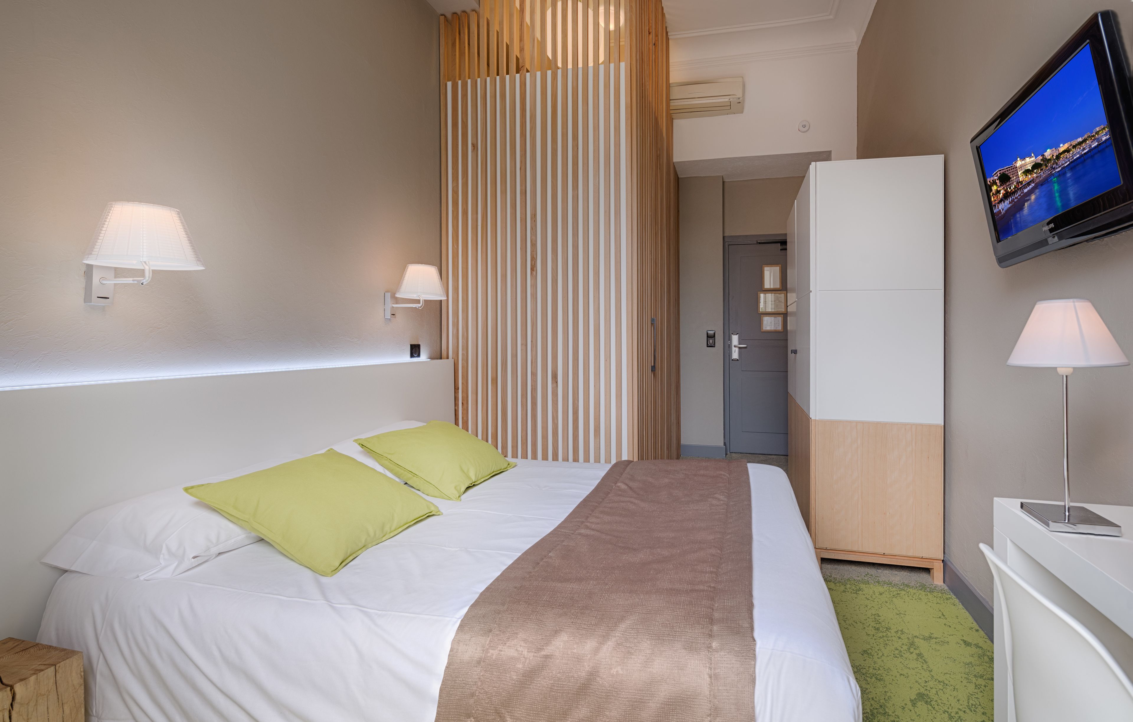 A hotel room with a bed, two bedside lamps, a television, and a wardrobe.