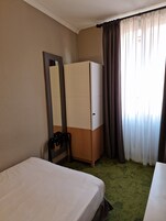 Een hotelkamer met een bed, een kledingkast, een spiegel en een raam met gordijnen.
