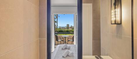 A modern bathroom with a large mirror, a bathtub, and a view of an outdoor seating area.