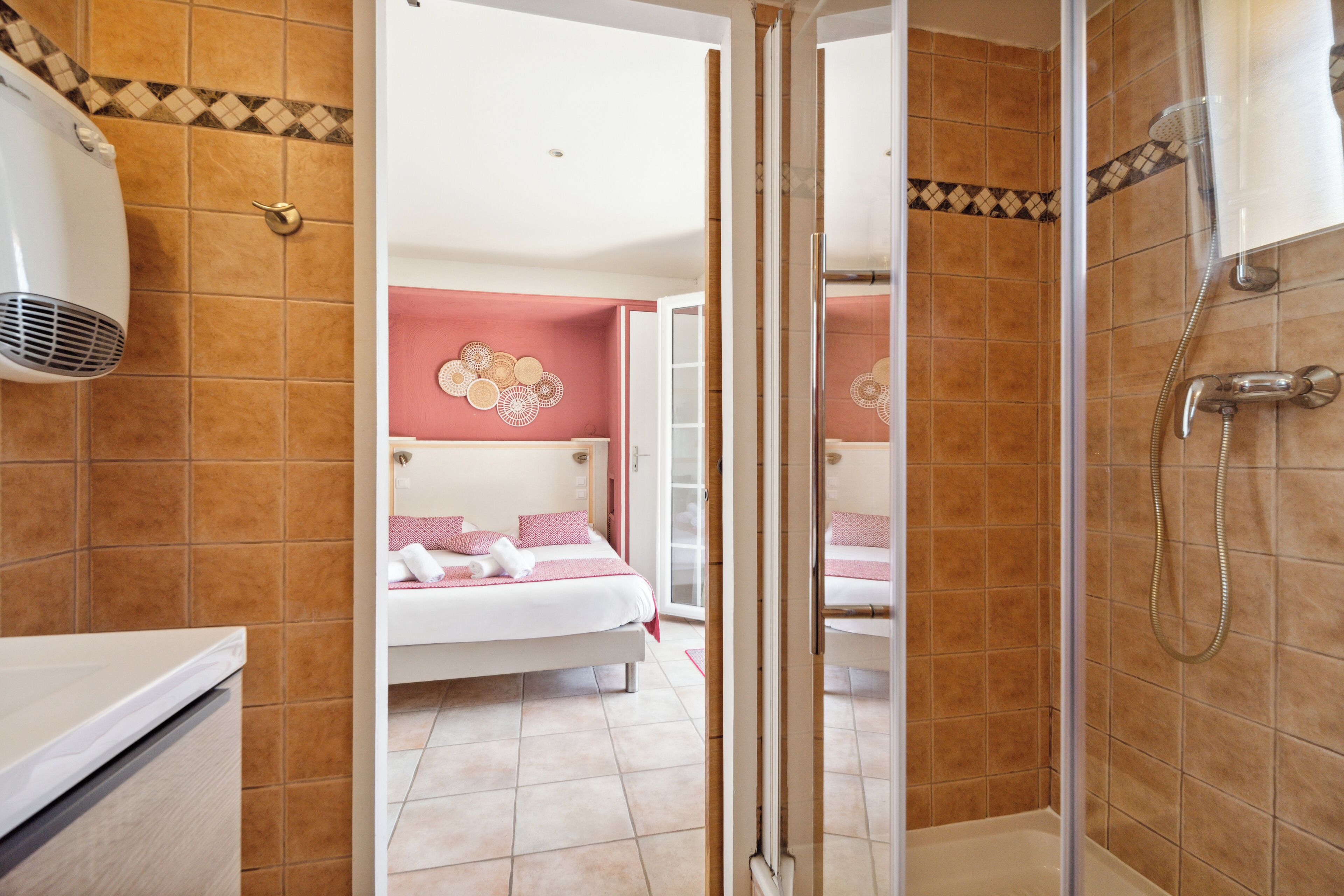 A hotel room with a shower, a bed with pink bedding, and a decorative wall.
