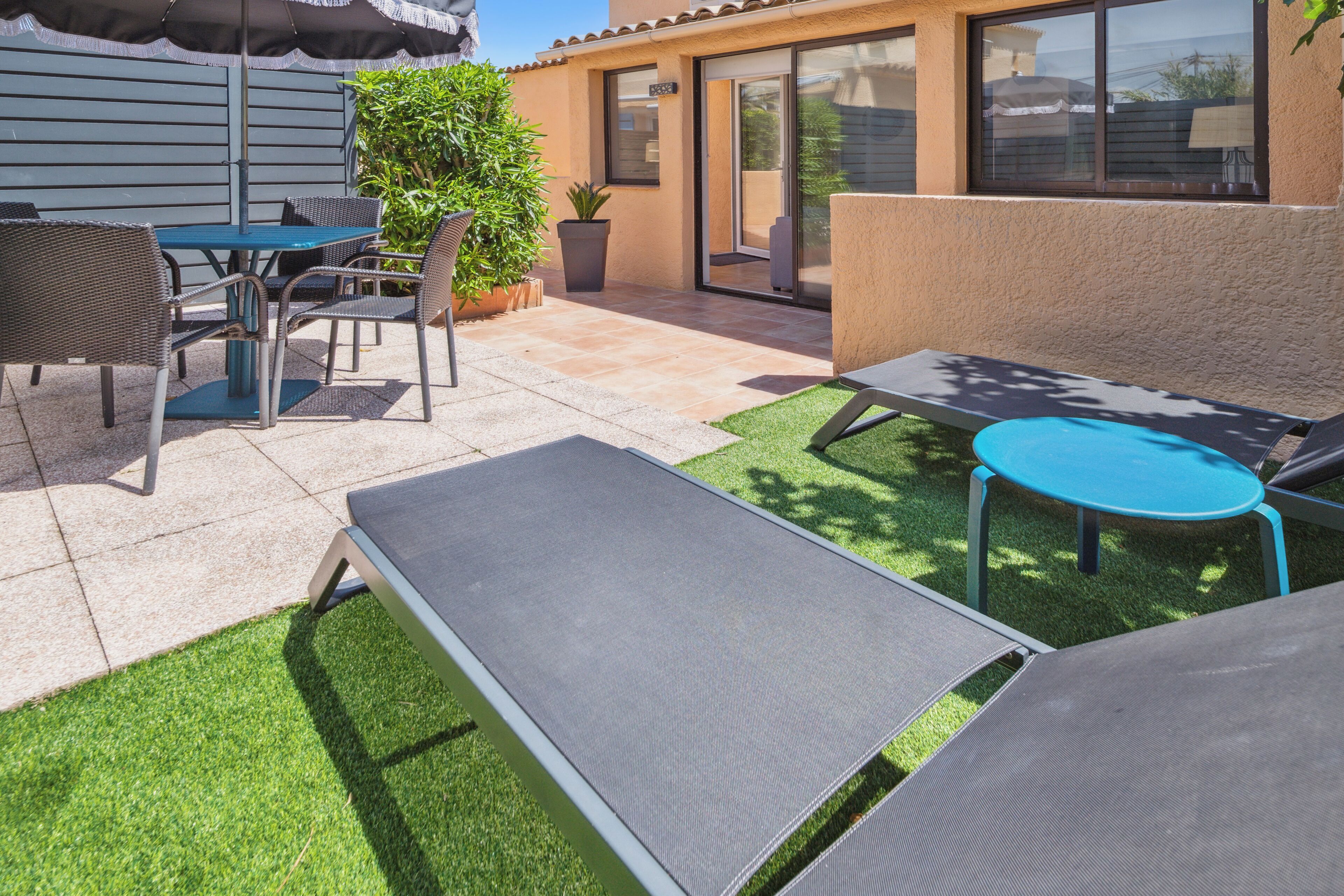 Un patio con mobiliario exterior, que incluye una mesa y sillas, además de un área de descanso con un banco y una mesita.