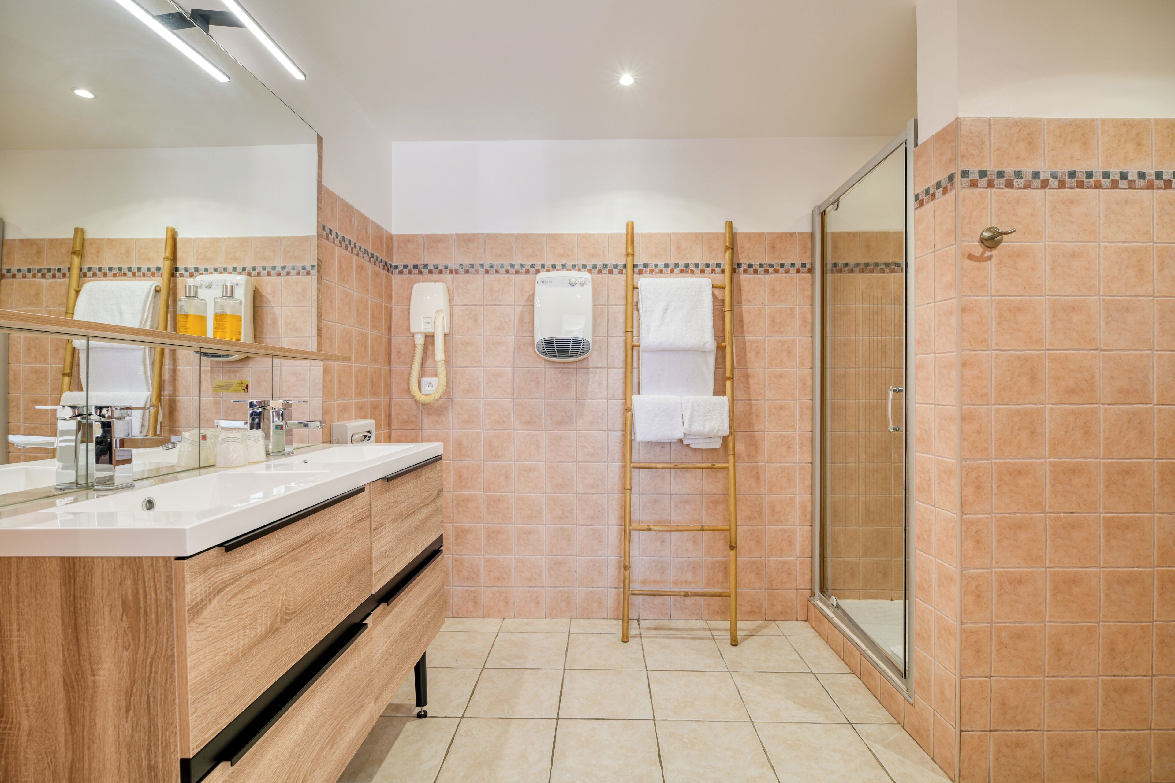 A bathroom with a wooden vanity, a glass shower enclosure, and a tiled floor.