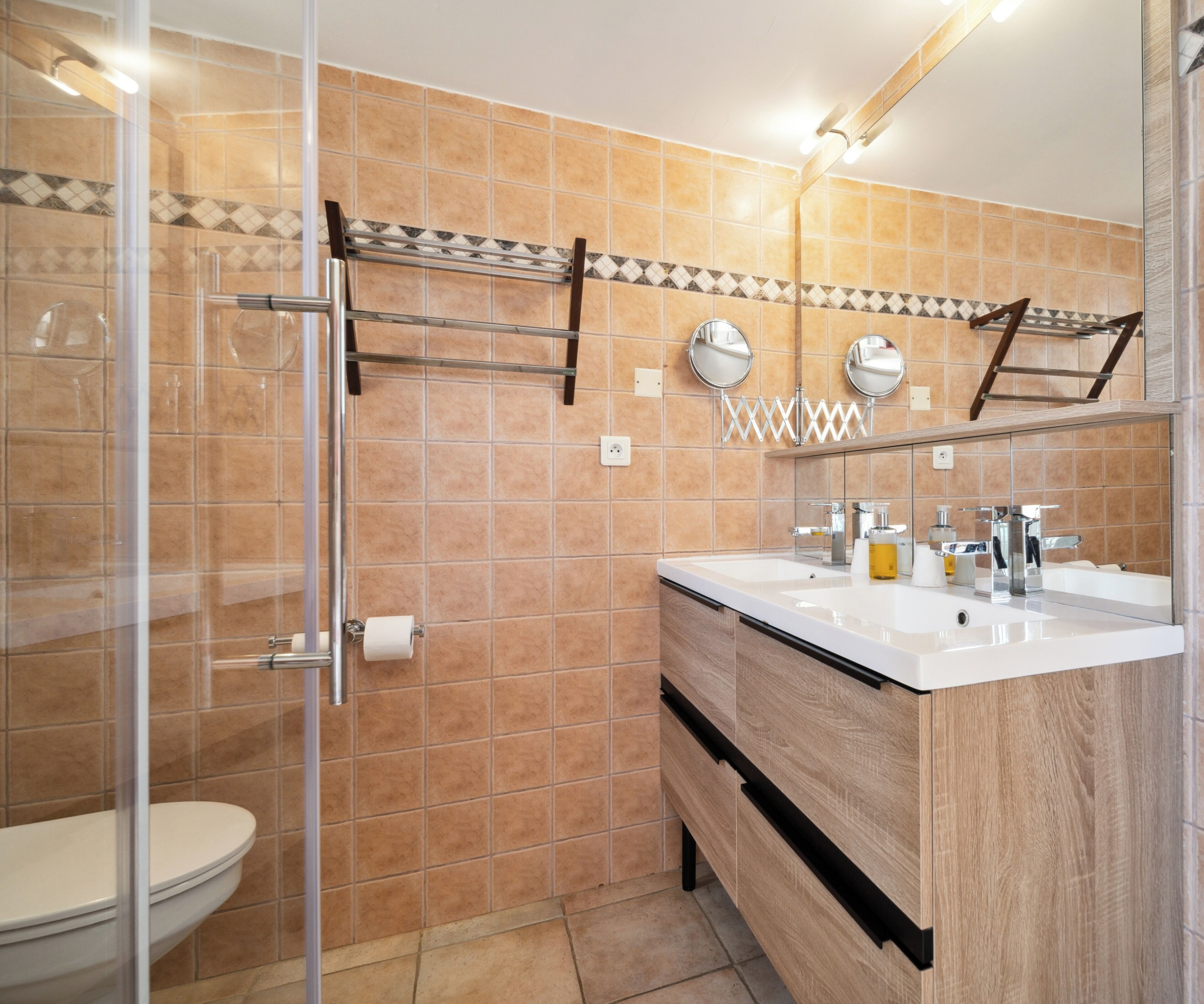 A modern bathroom with a glass shower enclosure, a toilet, a sink with a mirror, and a vanity with a wooden cabinet.