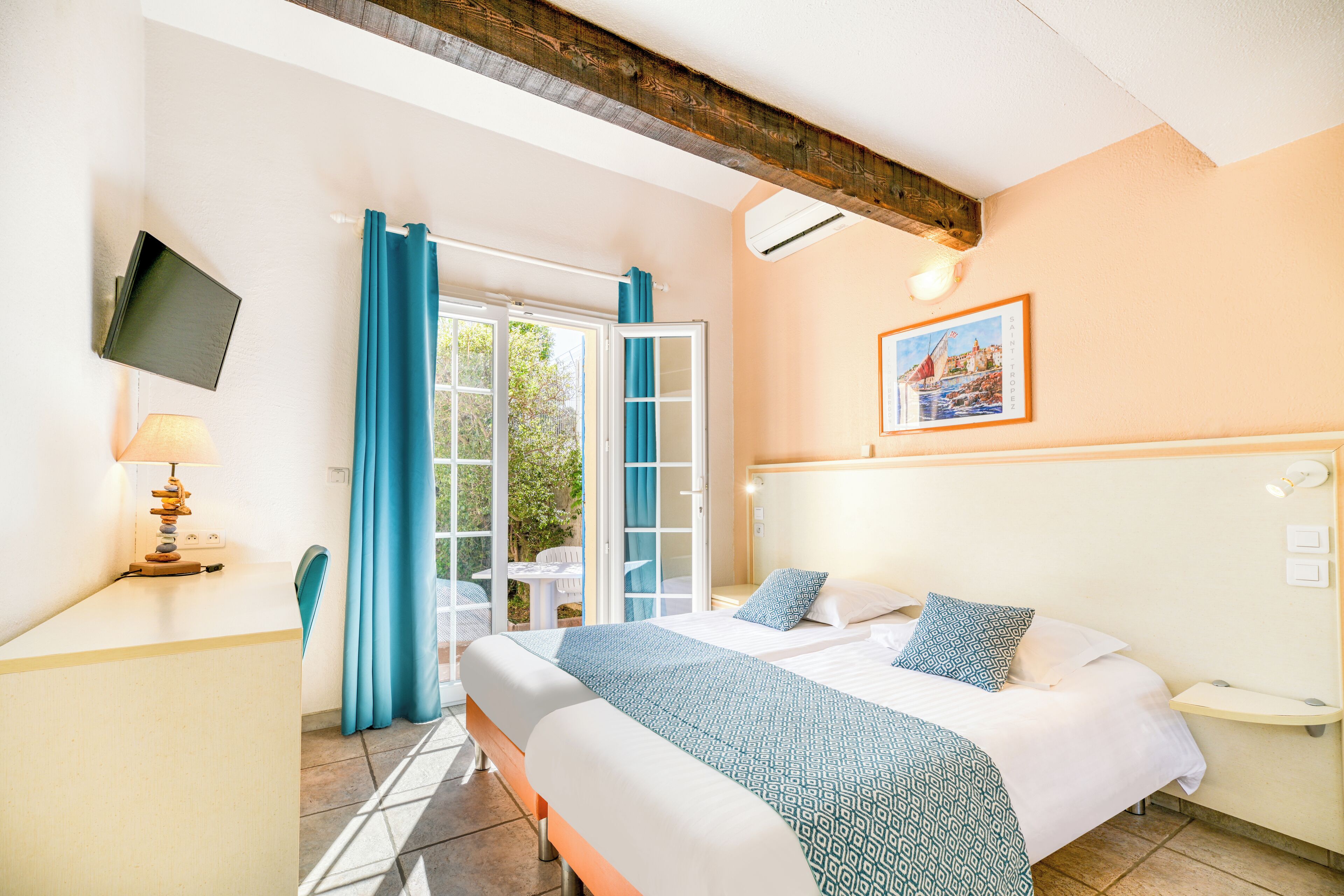 Habitación de hotel con cama, escritorio, silla, televisión y ventana con cortinas.