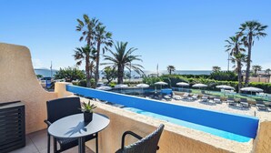 A rooftop pool area with lounge chairs and umbrellas, overlooking a beach and ocean. - Hôtel La Nartelle (Sainte-Maxime)