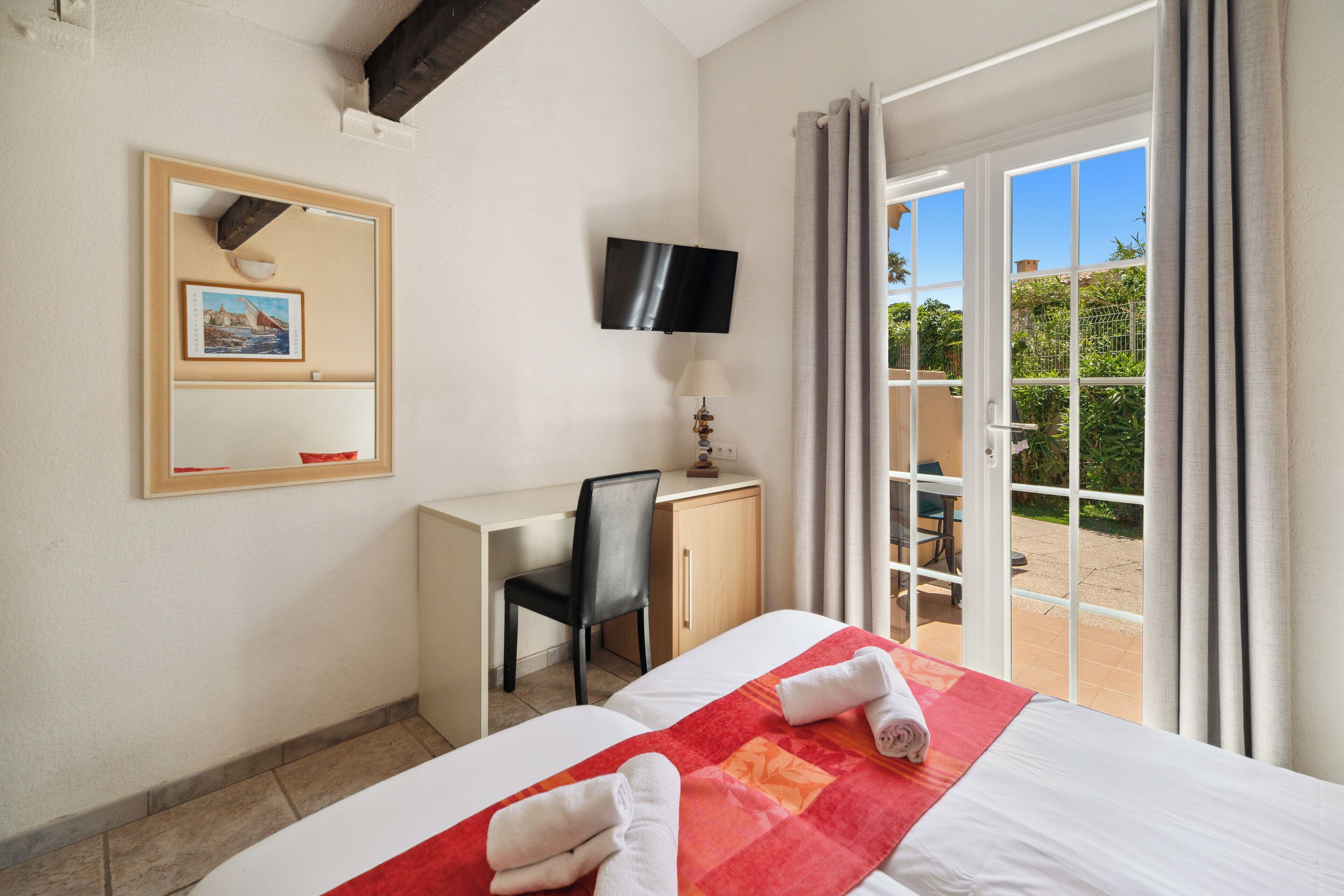 Ein Hotelzimmer mit einem Bett, einem Schreibtisch, einem Sessel, einem Fernseher und einer Glastür zum Balkon.