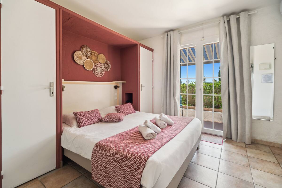 Ett hotellrum med en säng, en dekorativ väggdekoration, ett fönster med gardiner och utsikt över grönområden utanför.