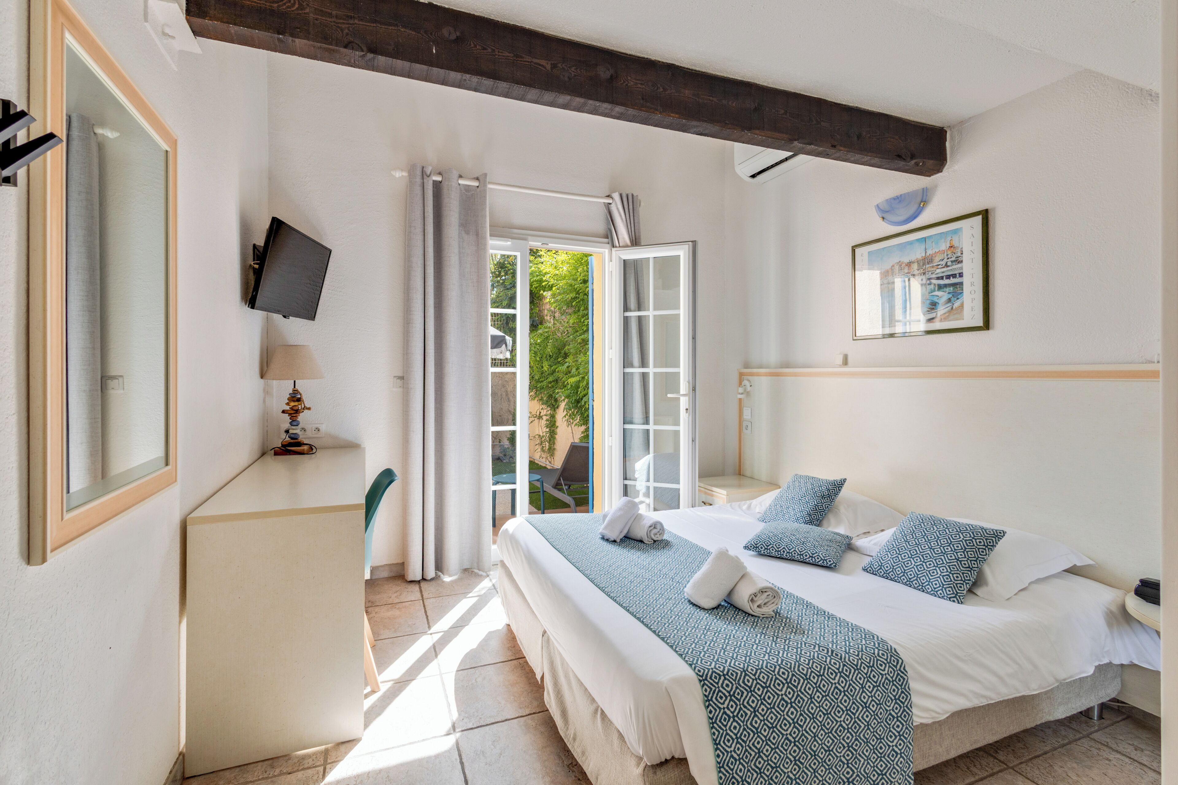 Une chambre à coucher comprenant un lit, une télévision, un bureau et une porte donnant sur un espace extérieur.