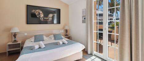 A hotel room with a large bed, two bedside tables with lamps, a framed artwork on the wall, and a view through a glass door to the outside.