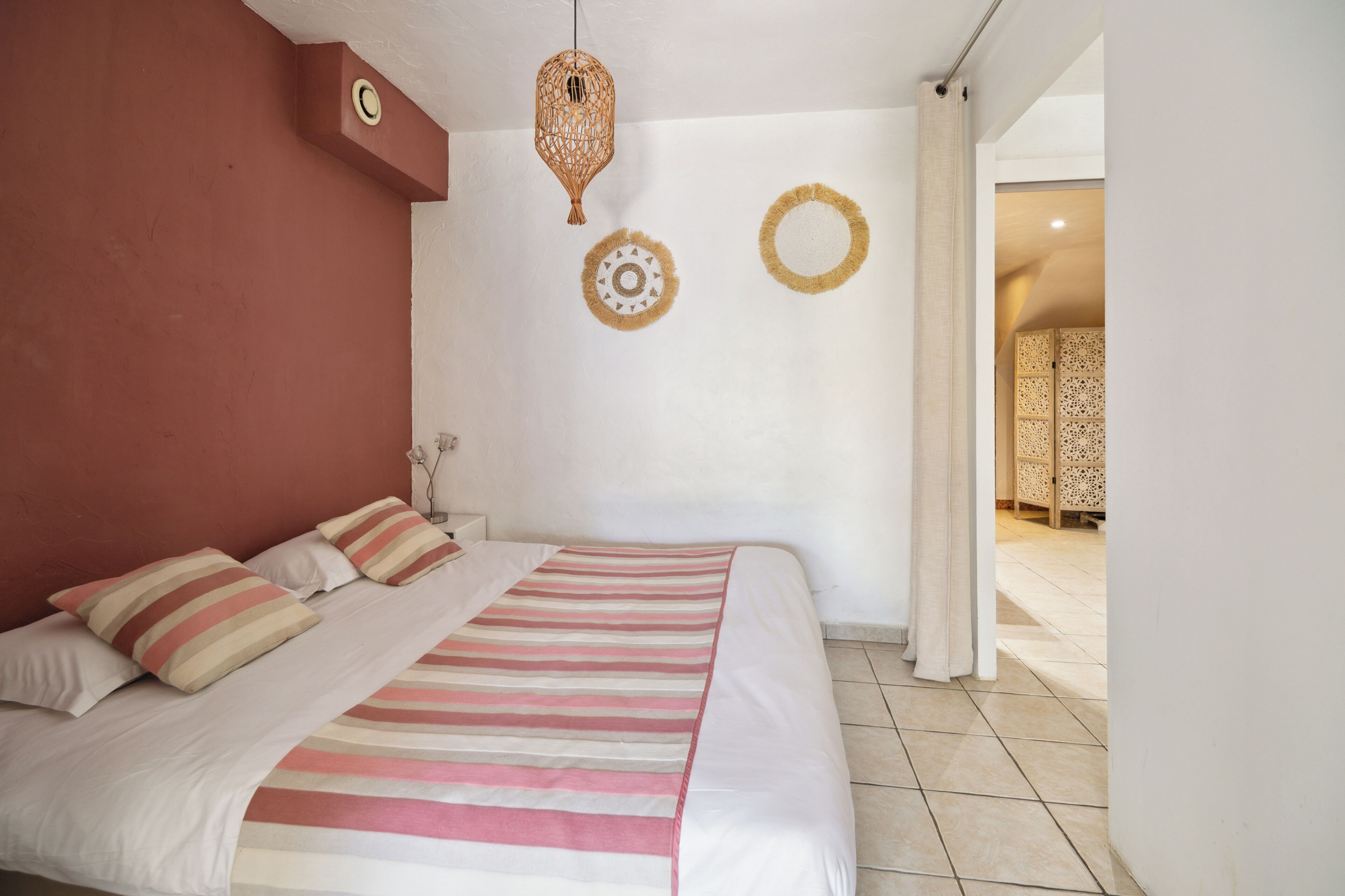 A bedroom with a bed, pillows, a hanging light fixture, and two wall decorations.