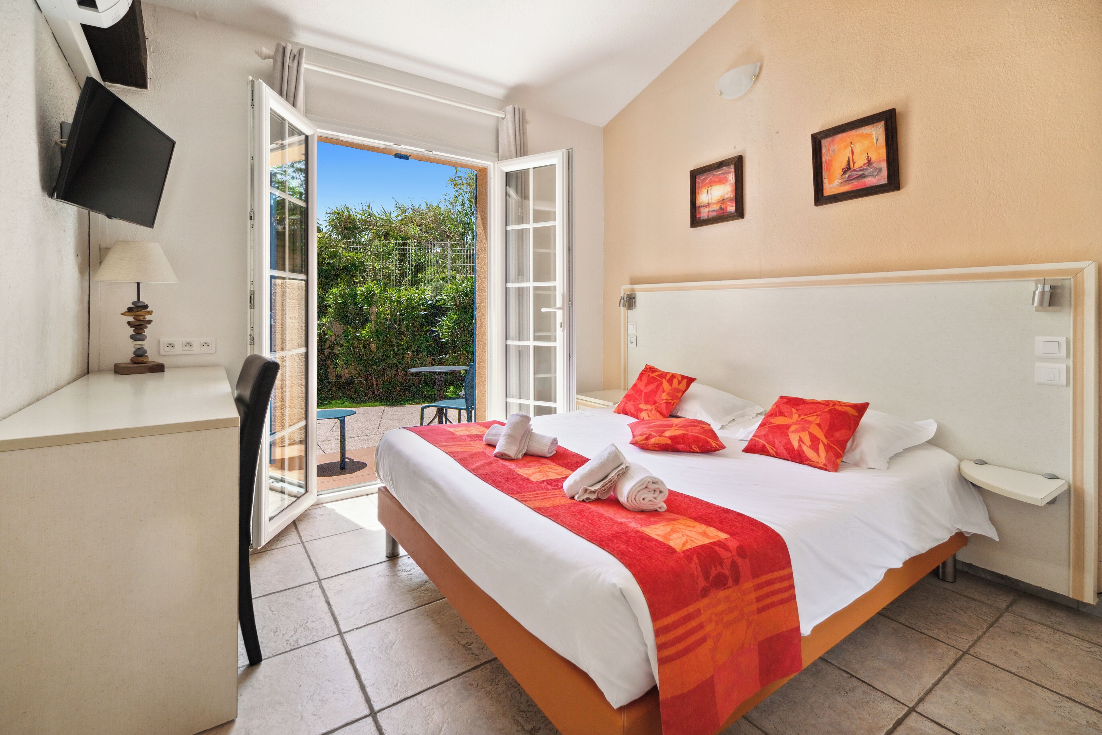 Una habitación de hotel con cama, escritorio, silla y televisor montado en la pared.