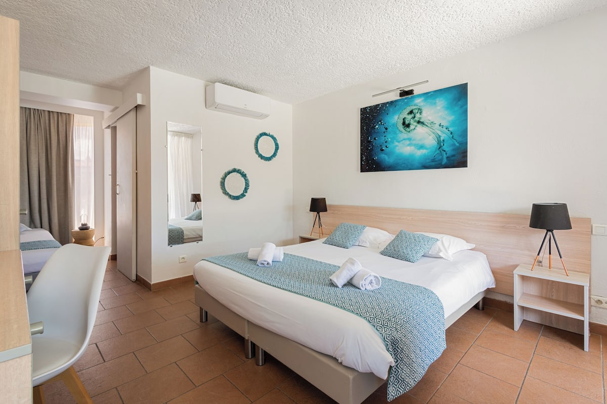 Ett hotellrum med en stor säng, ett skrivbord, en stol, en spegel och en tavla på väggen.