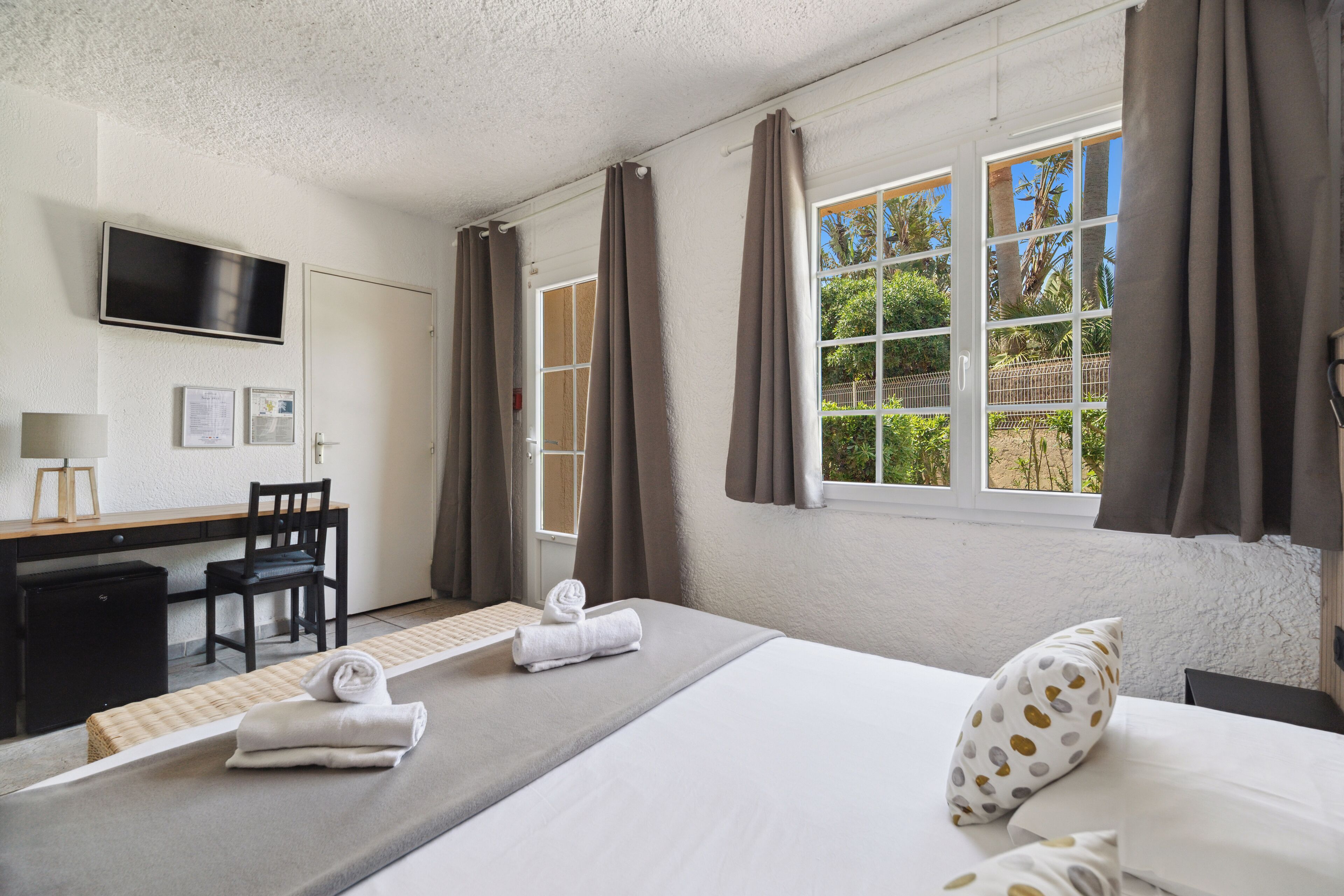 A hotel room with a bed, a desk, a chair, a TV, and a window with curtains.